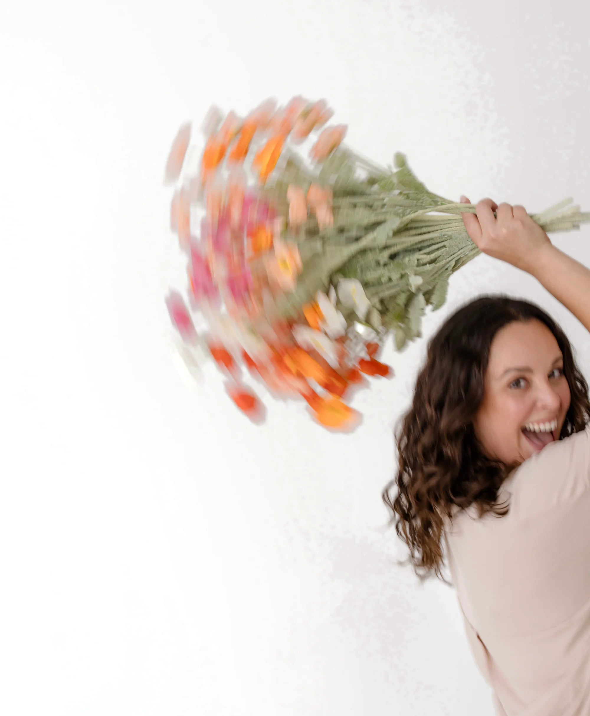 Marisa riendo mientras gira un ramo de flores naranjas y rosas; el ramo sale movido por la velocidad.
