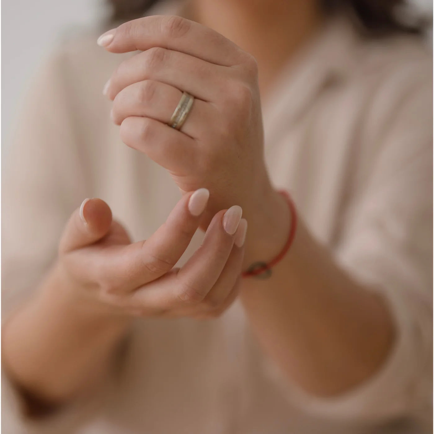 Las manos de una mujer sosteniéndose una a la otra, con una pulsera roja en la muñeca.