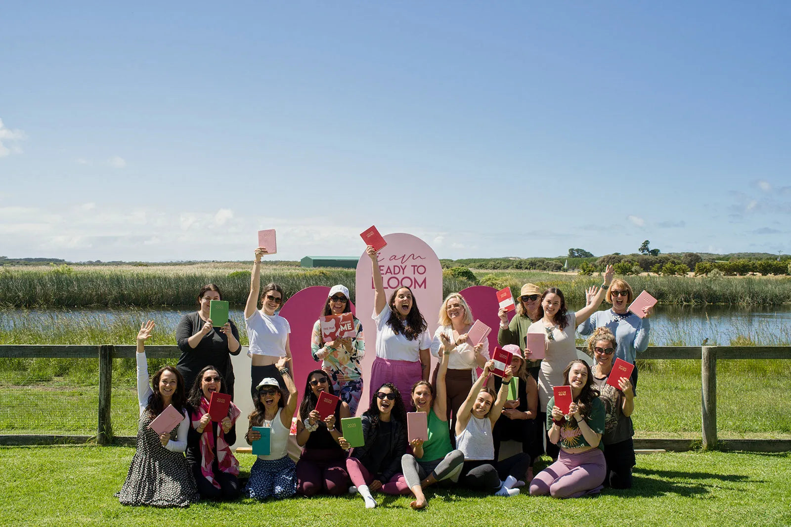 Una veintena de mujeres al aire libre levantando sus planners delante del arco de I Am Ready To Bloom.