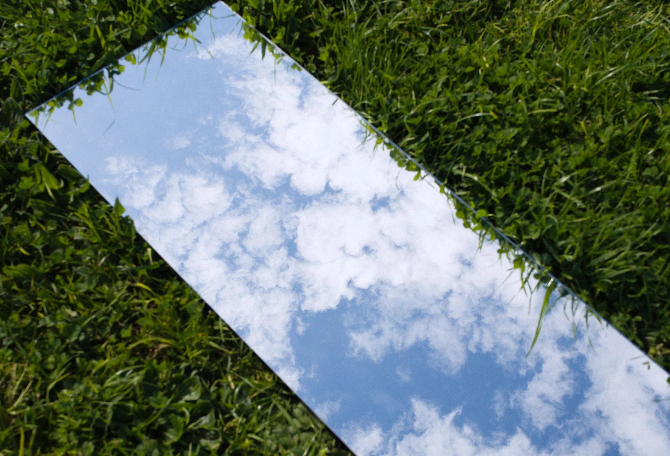 Un espejo alargado tirado sobre el pasto, reflejando un cielo con nubes.